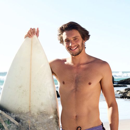 surf-guy-standing-with-surfboard-at-the-beach-P3E48SA.jpg